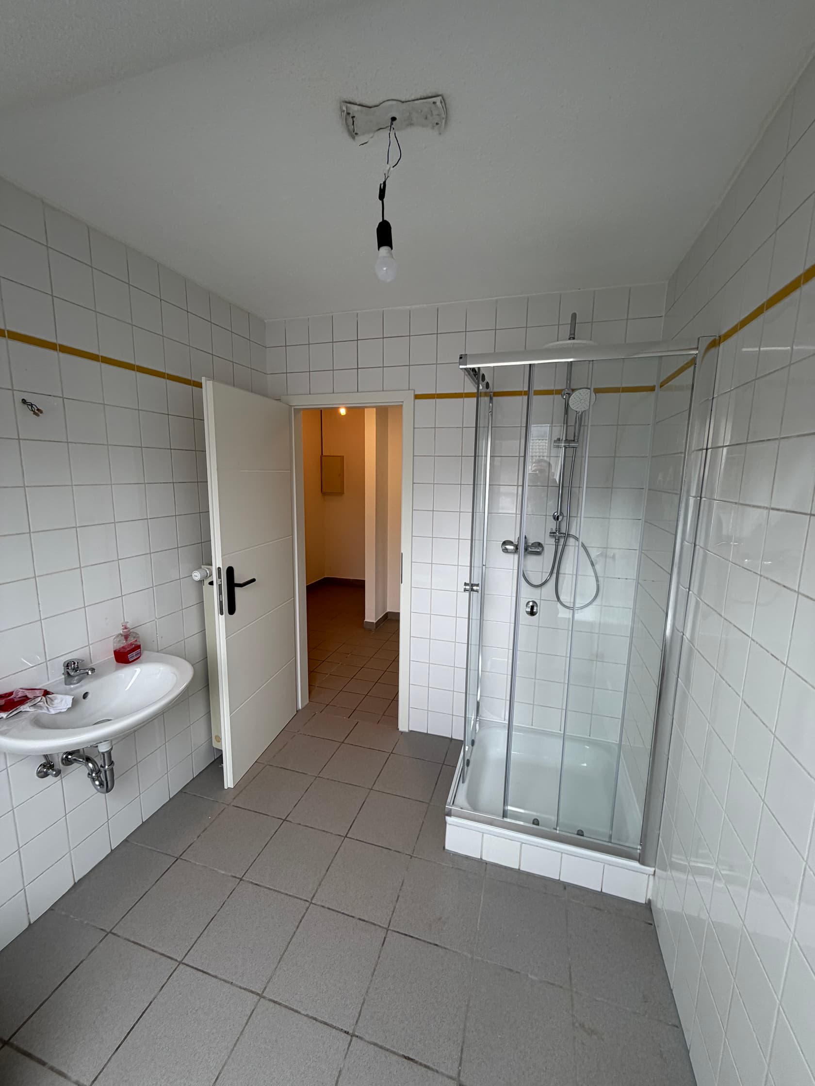 Weiß gefliestes Bad mit Eckdusche, Waschbecken und grauem Bodenbelag